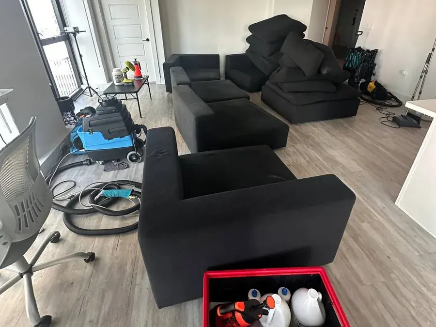 The sectional taken apart during cleaning, cushions stacked, with a hot water extractor