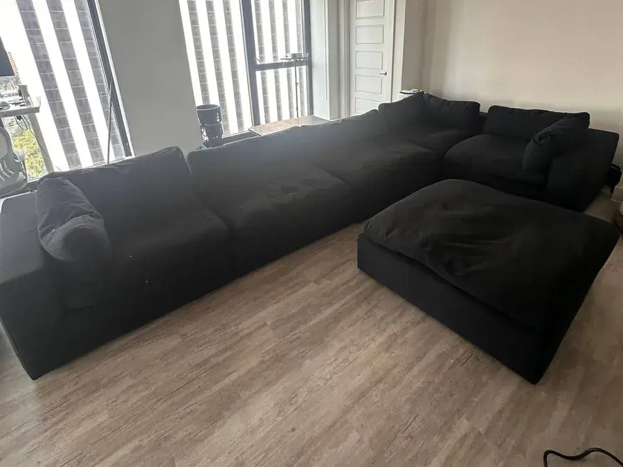 Large black modular sectional and ottoman before cleaning in a Houston high-rise apartment