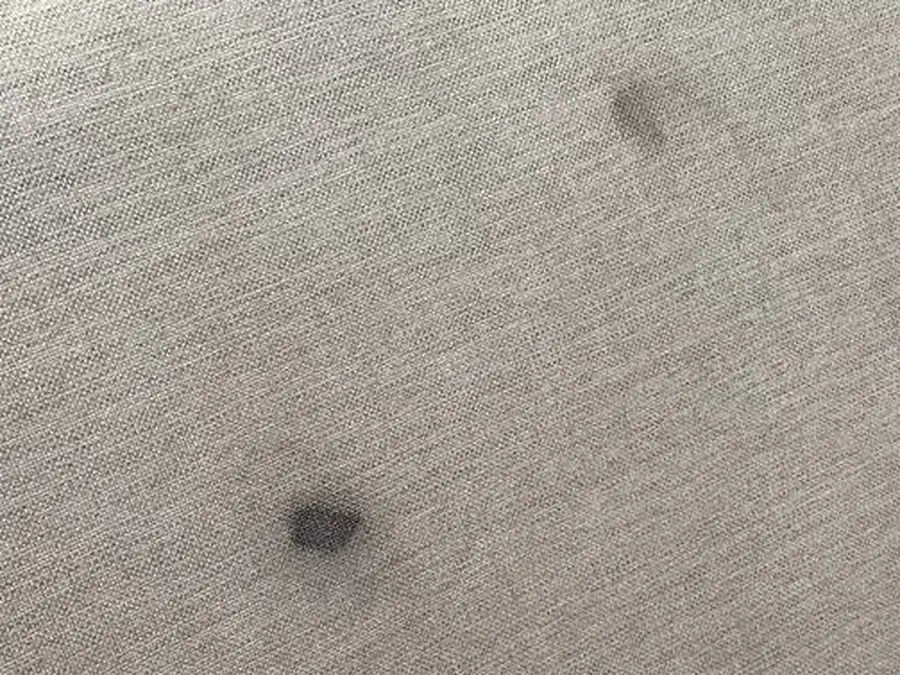 Two dark ink marker stains on a gray woven sectional back cushion before cleaning