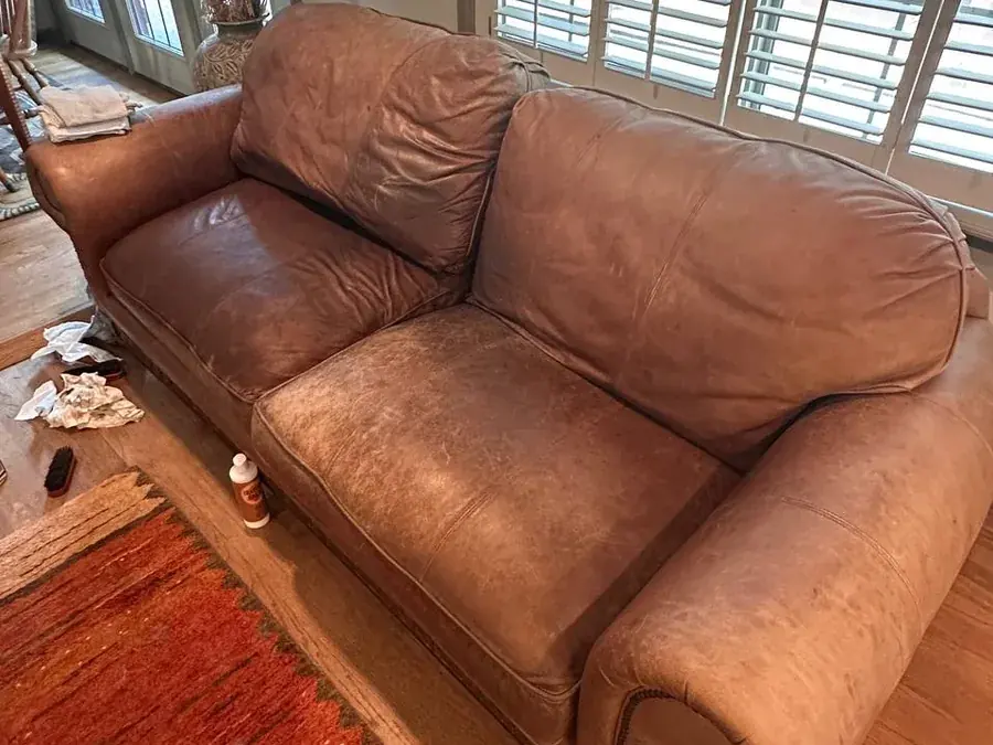 Brown leather sofa before cleaning, faded and scuffed with dirt and stains, in a Houston home