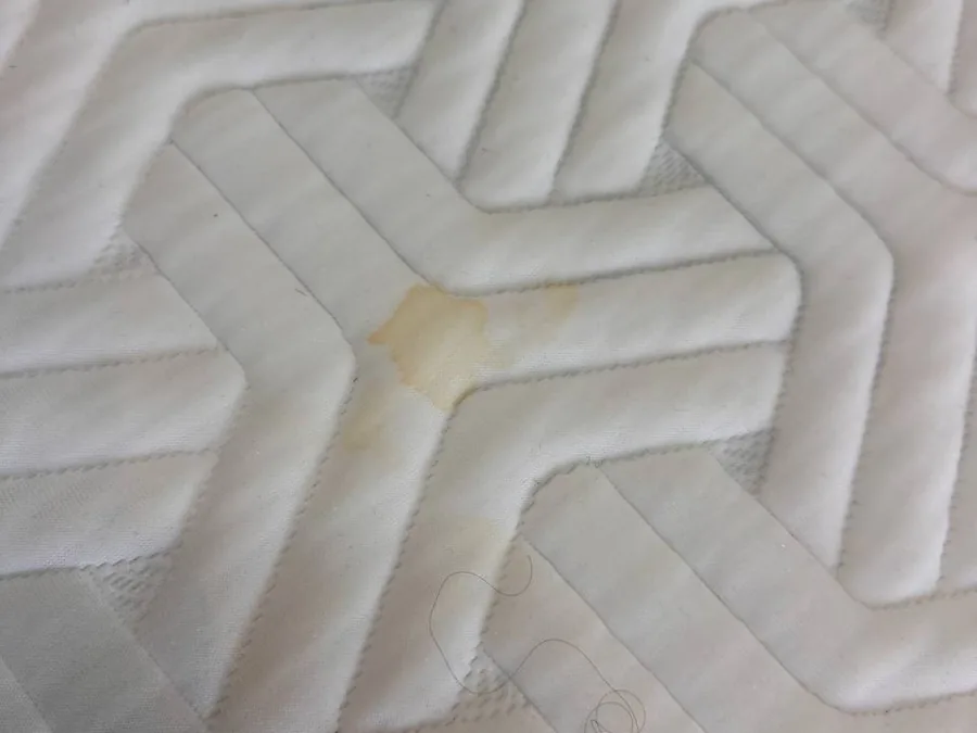 Close-up of a yellow organic stain on a quilted mattress cover before cleaning