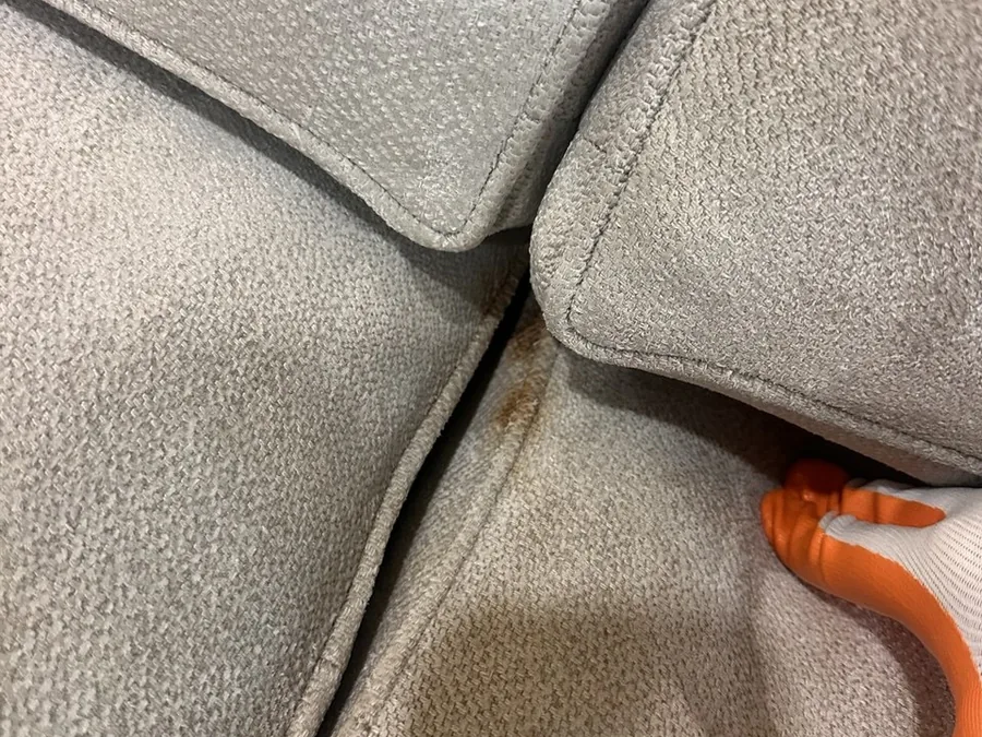 Close-up of a greasy food stain in the seam between seat cushions before cleaning