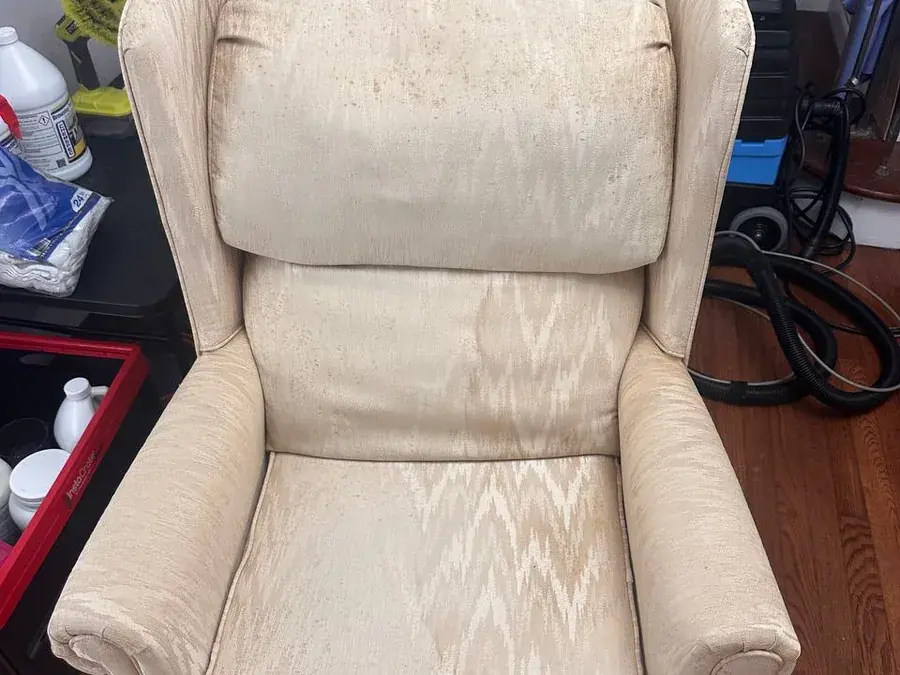 Cream wingback armchair before cleaning, covered in rust-colored water stains and dirty rings